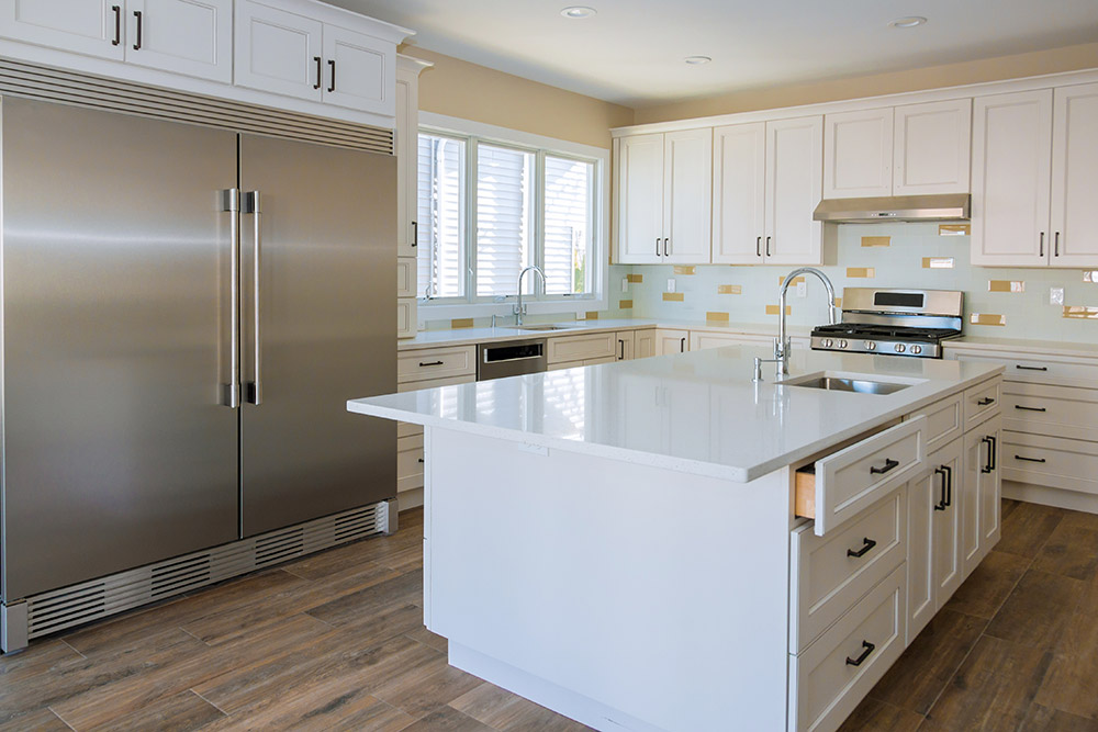 A large kitchen with an island that has a sink, and a large industrial-sized fridge.